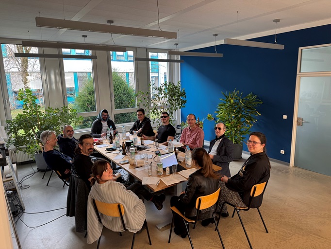 Foto der Abteilung Softwareentwicklung. 3 Damen und 9 Herren sitzen an einem Tisch und lächeln in die Kamera. Manche von ihnen sind verkleidet. Sie spielen gerade eine Mörderische Dinnerparty.